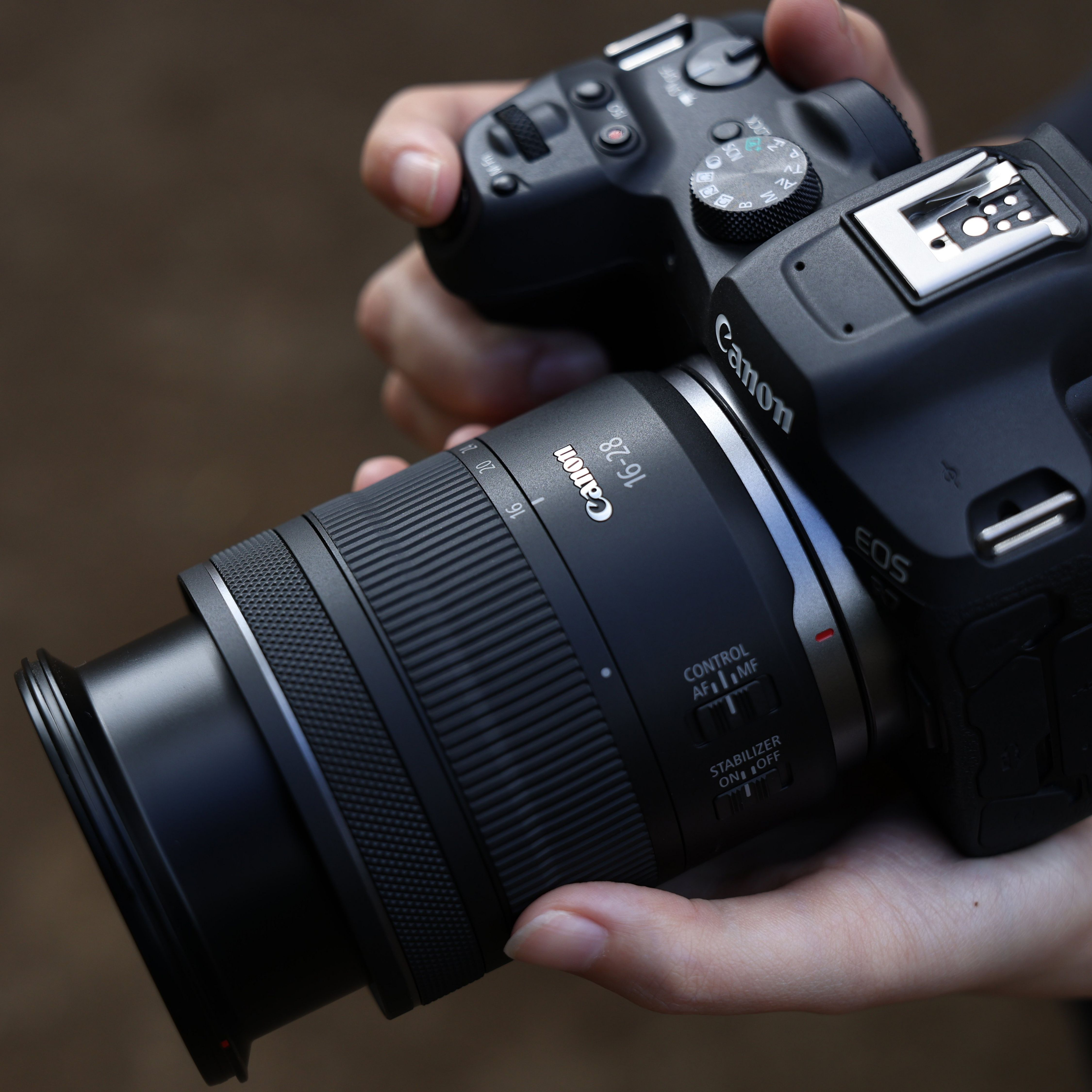 Des mains tiennent un appareil photo Canon EOS noir avec un objectif 16-28mm.
