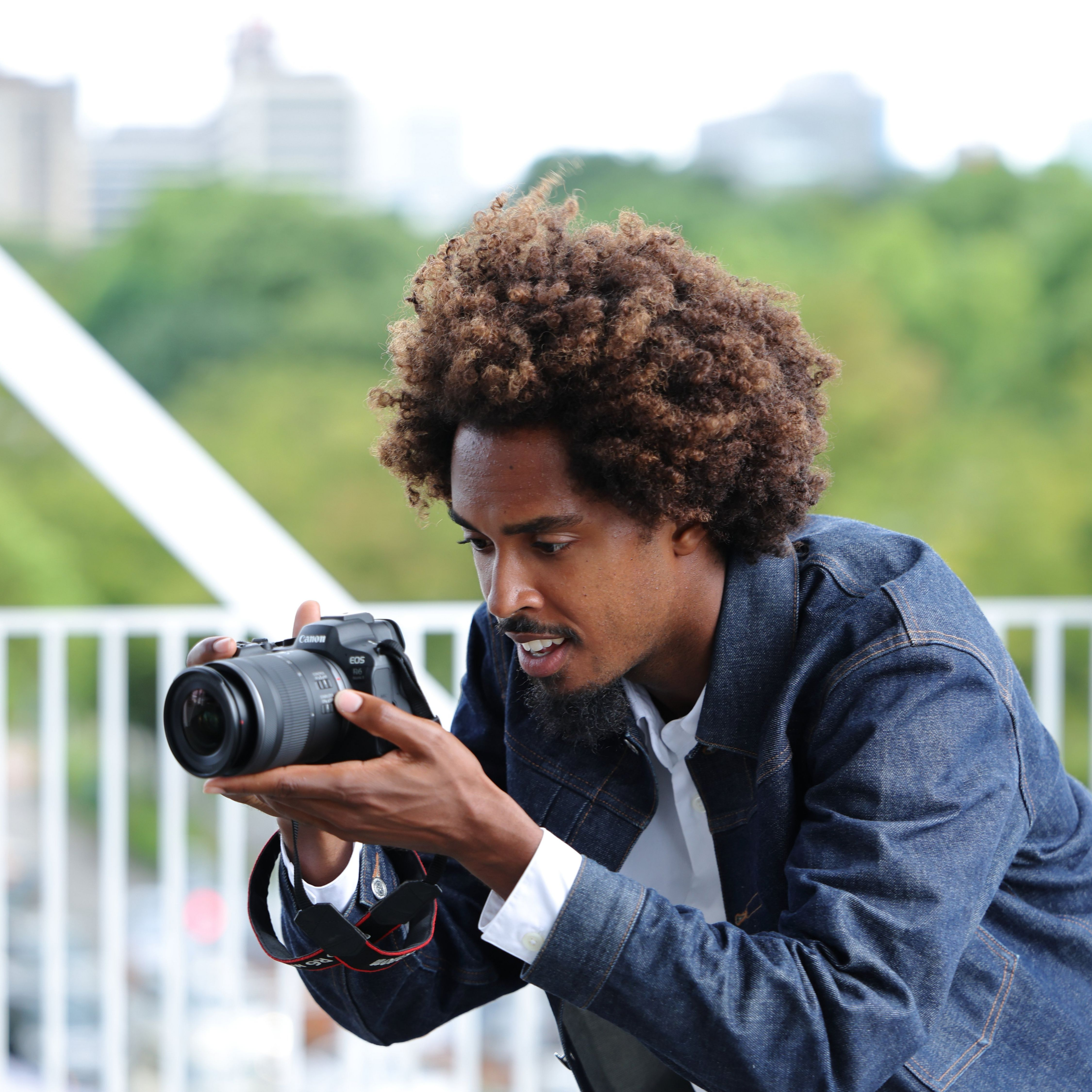 Un homme aux cheveux bouclés tient un appareil photo et le regarde.