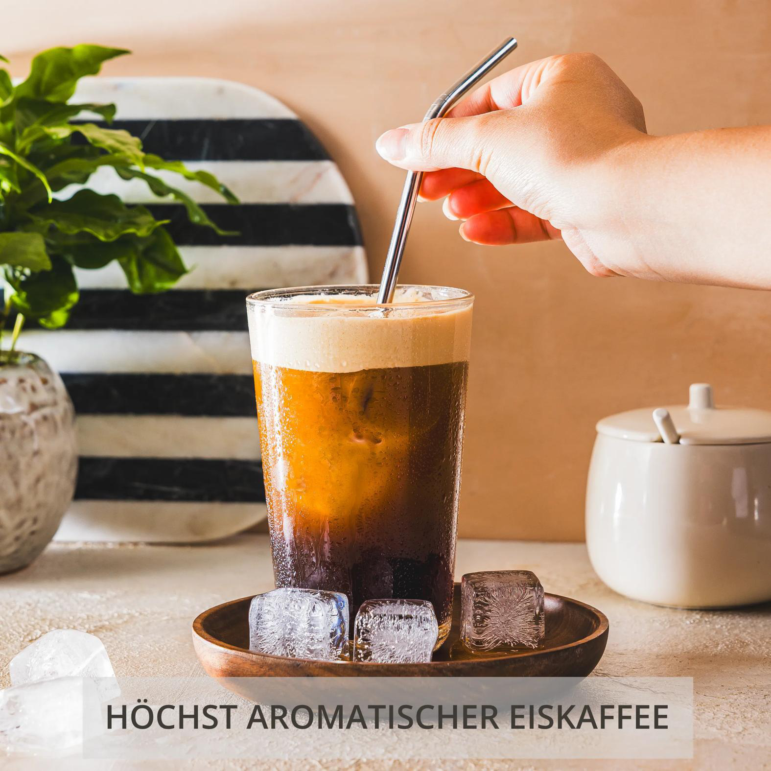 Ein Glas Eiskaffee mit Eiswürfeln und einem Strohhalm. Ein Zuckerbehälter steht daneben.