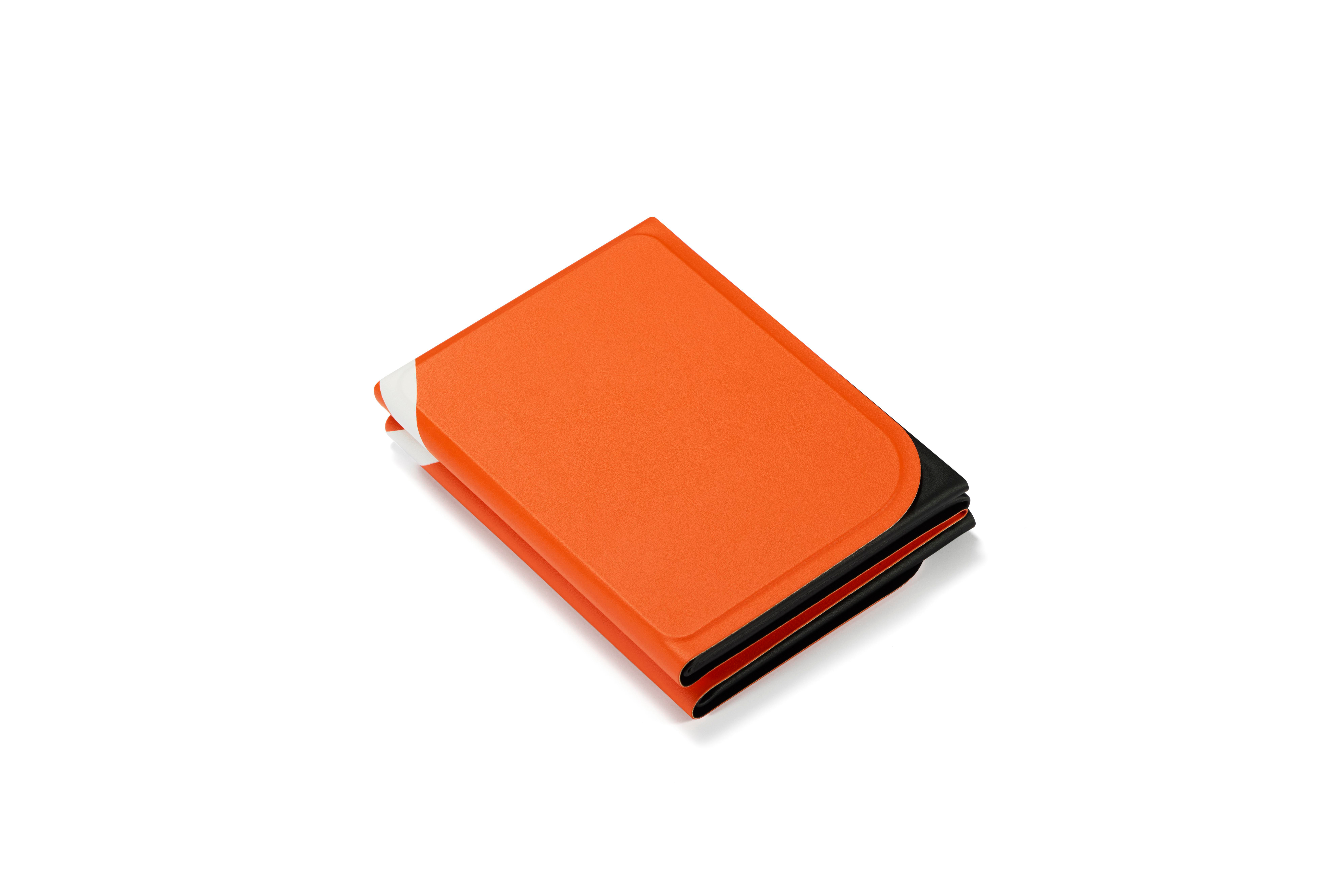 Ein orangefarbenes Buch mit schwarzen Seiten liegt auf einem weißen Hintergrund.
