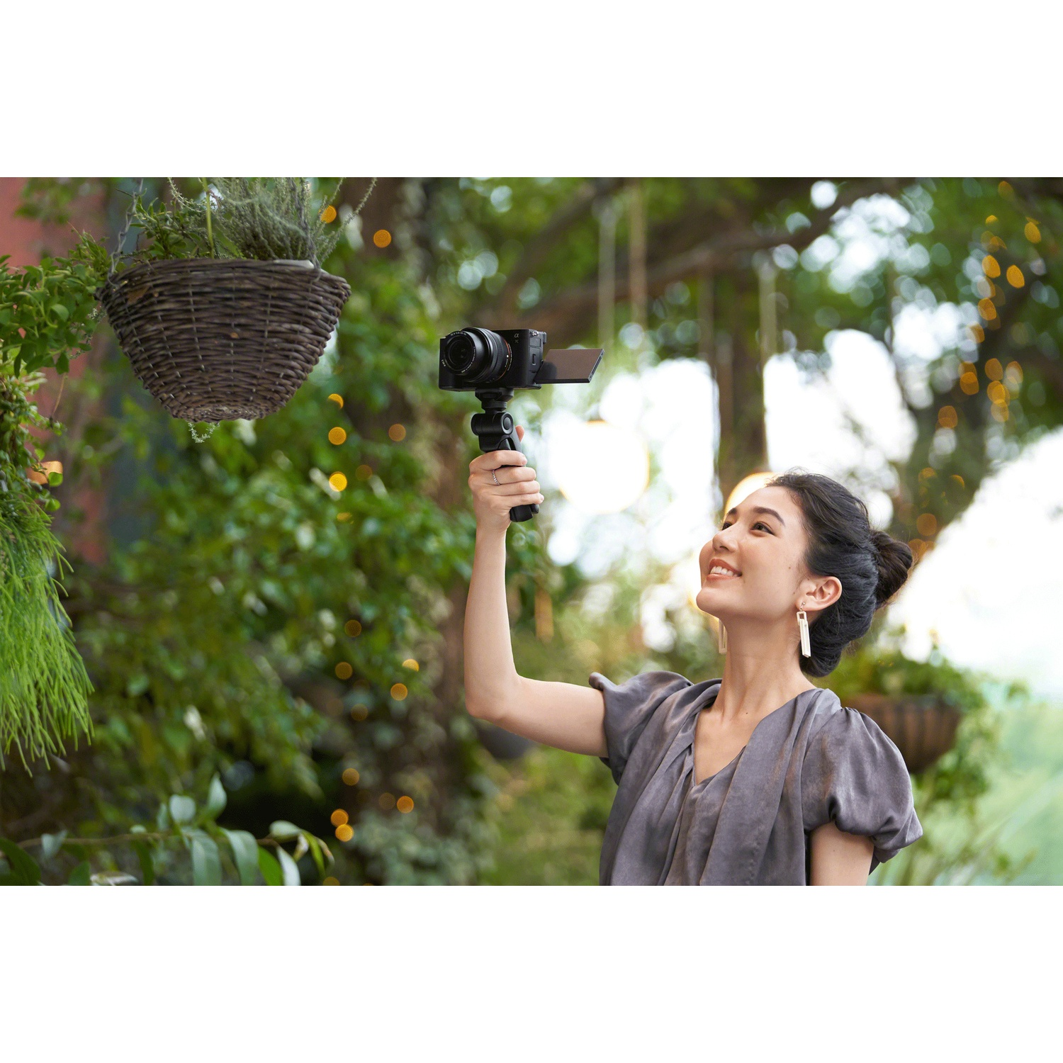 A woman holds a camera with a flip-out screen. She is smiling.