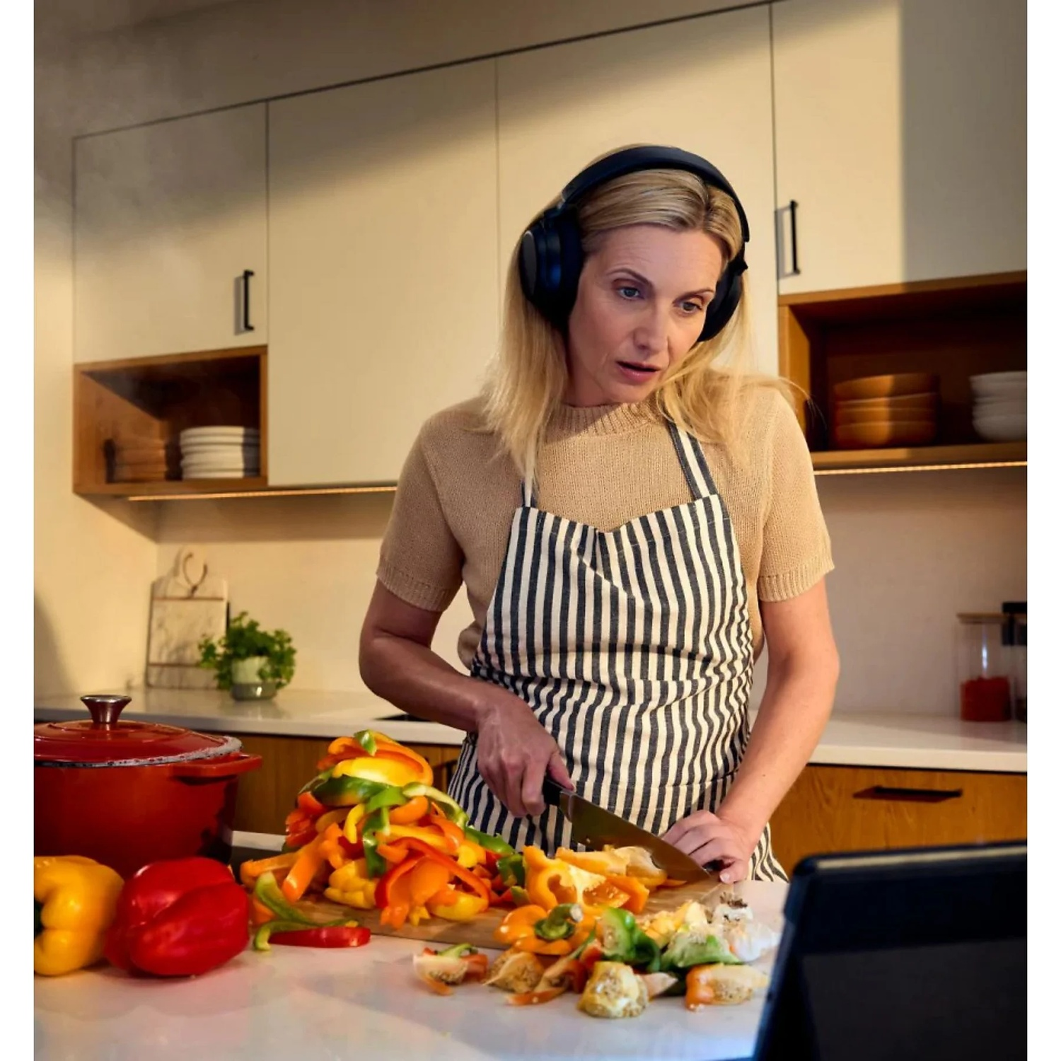 Une femme portant un casque et un tablier coupe des poivrons colorés dans une cuisine.