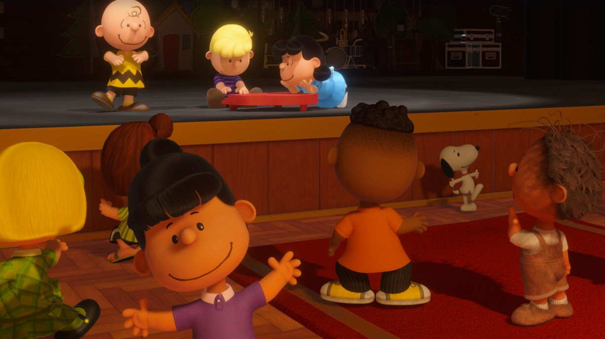 Charlie Brown und Freunde auf einer Bühne. Snoopy steht im Hintergrund.