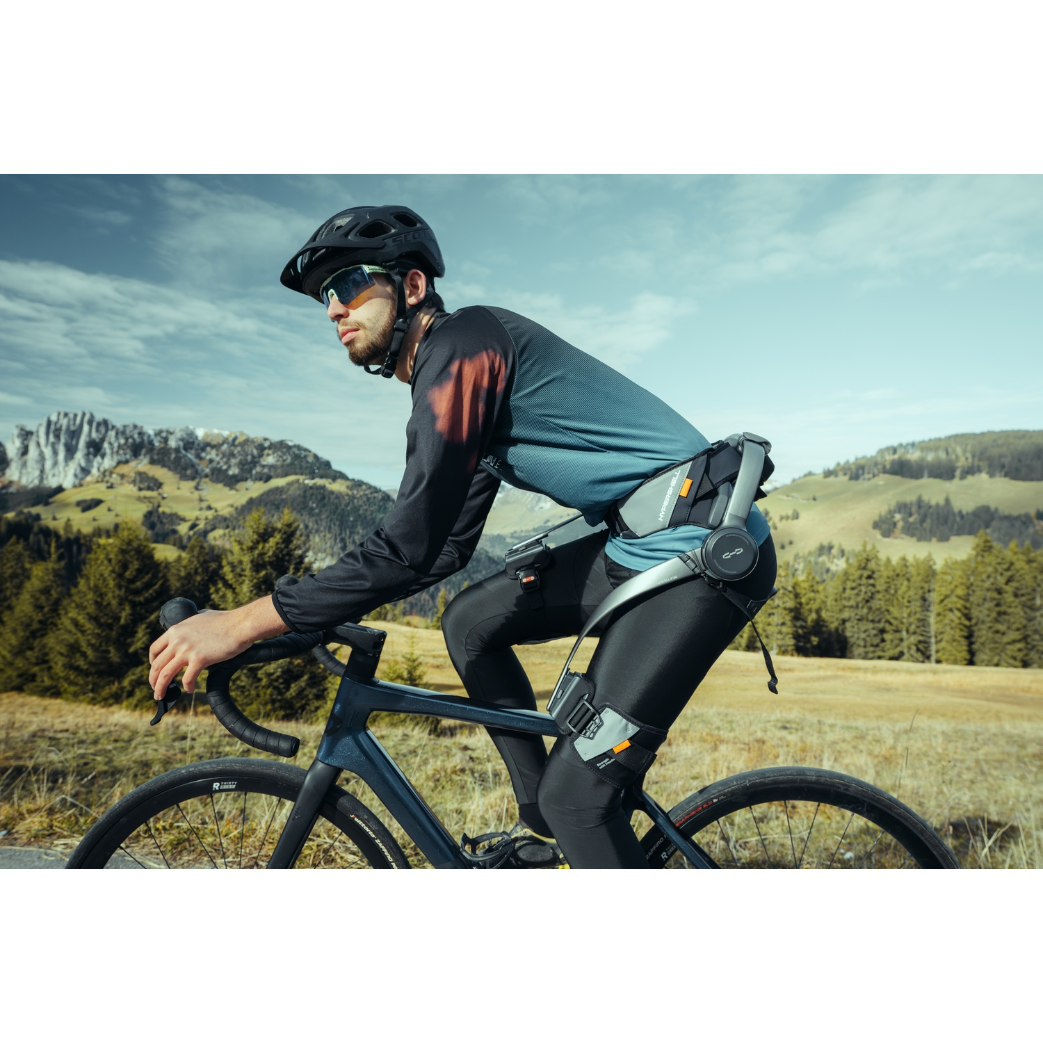 Un ciclista con esoscheletro pedala in un paesaggio montuoso.