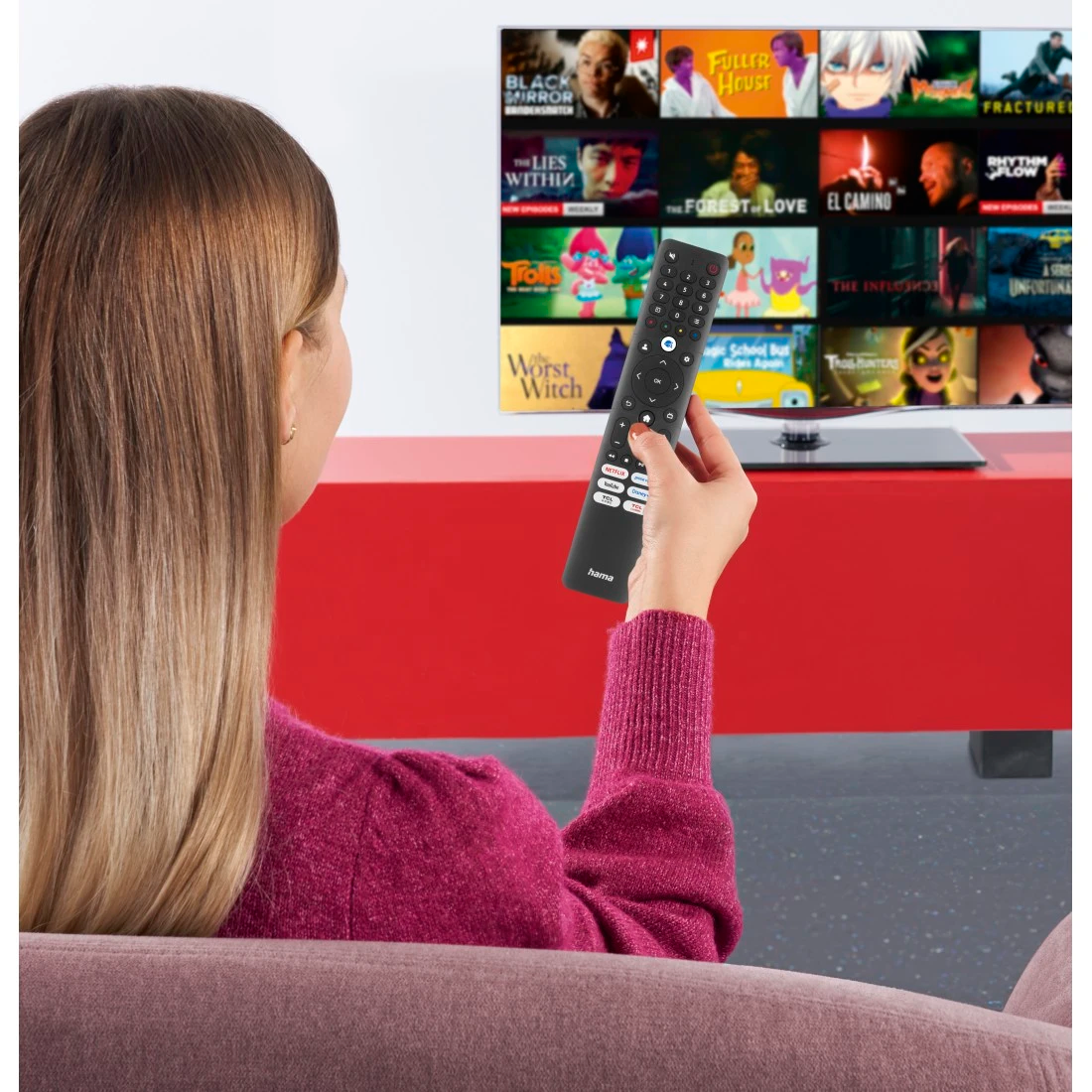 Egy nő távirányítót tart, és filmjavaslatokat megjelenítő TV-képernyőt néz.