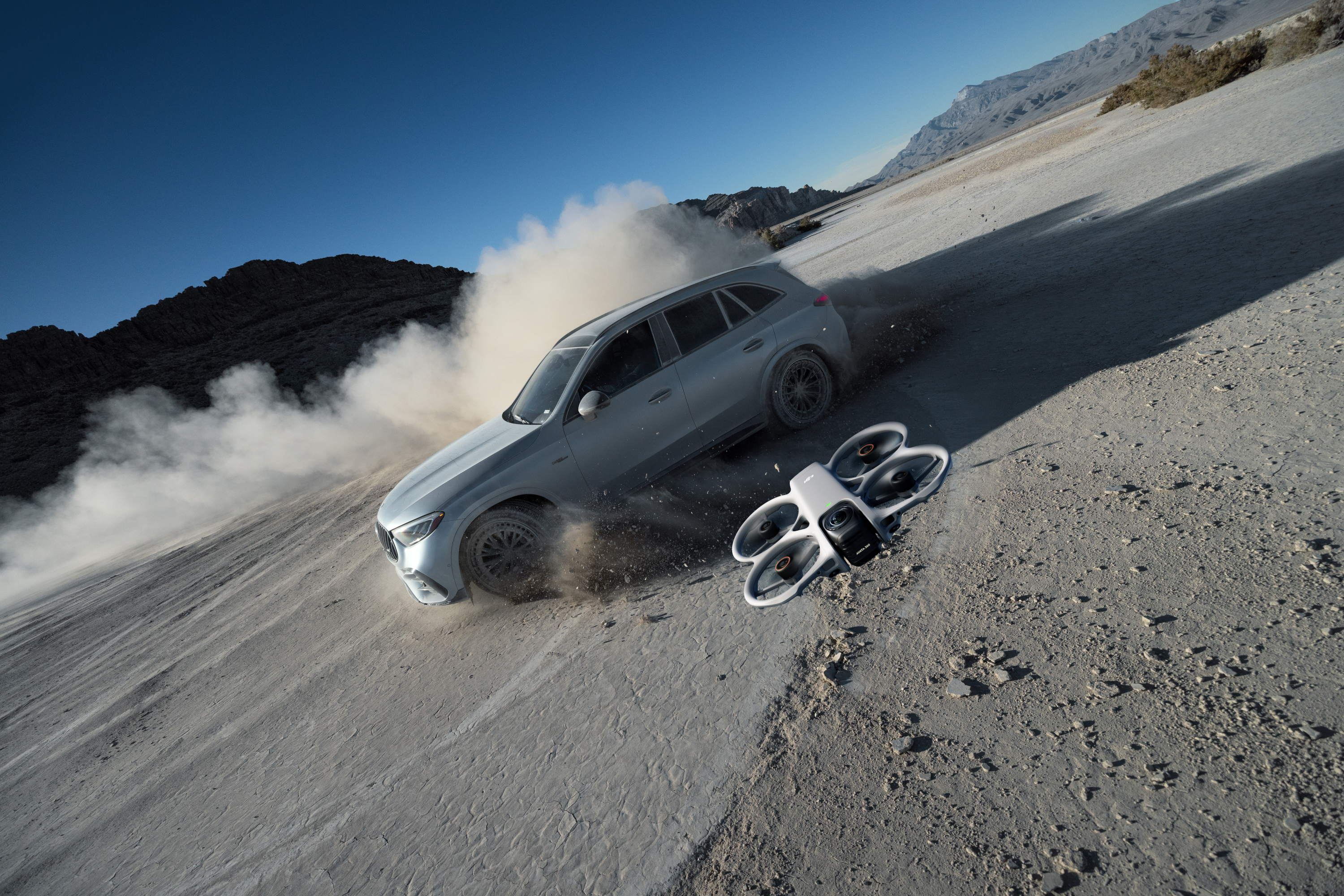 SUV argento fuoristrada solleva polvere, con un drone nelle vicinanze.