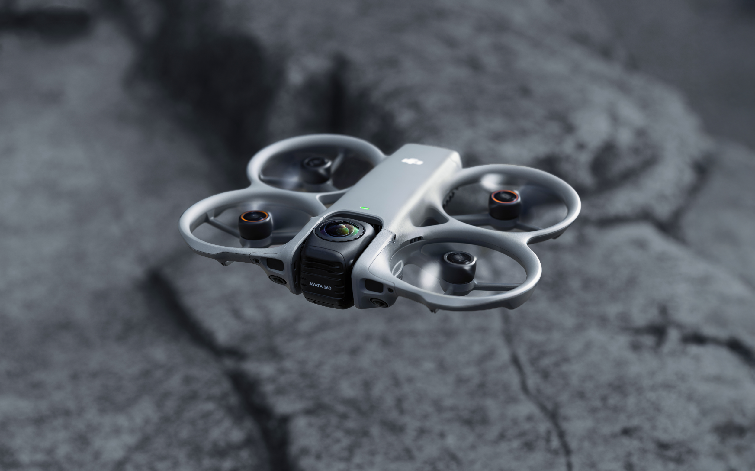 Un drone DJI Avata grigio vola davanti a uno sfondo roccioso sfocato.