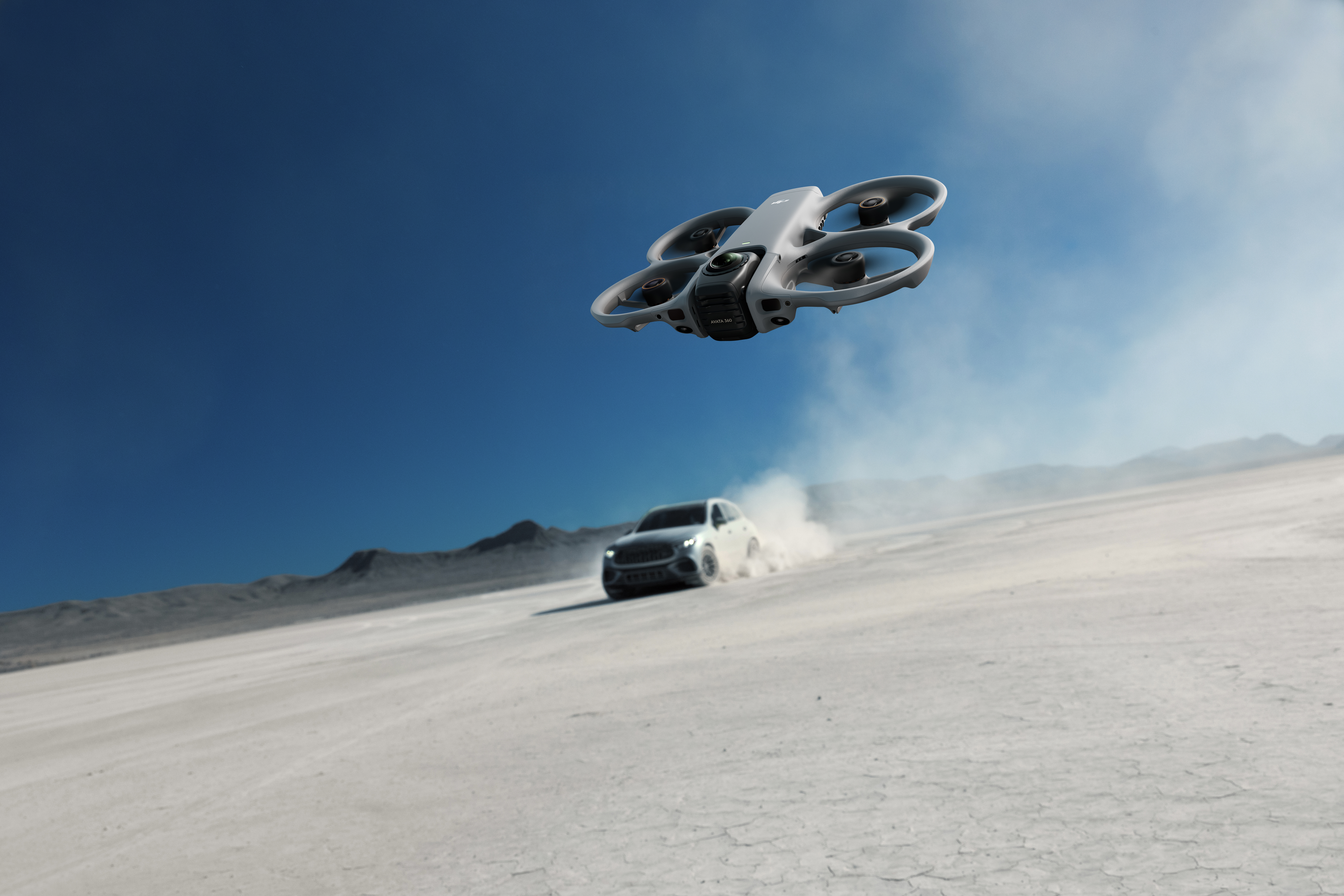Un drone vola sopra un'auto che solleva polvere.
