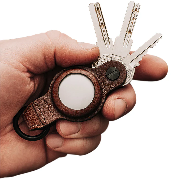Una mano tiene chiavi e un portachiavi in pelle con uno scomparto rotondo.