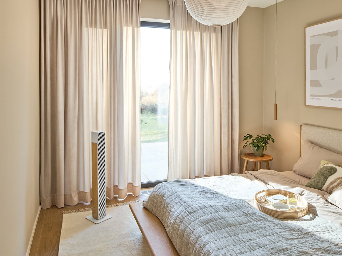 Ein Schlafzimmer mit Bett, Vorhängen und einem Turmventilator.