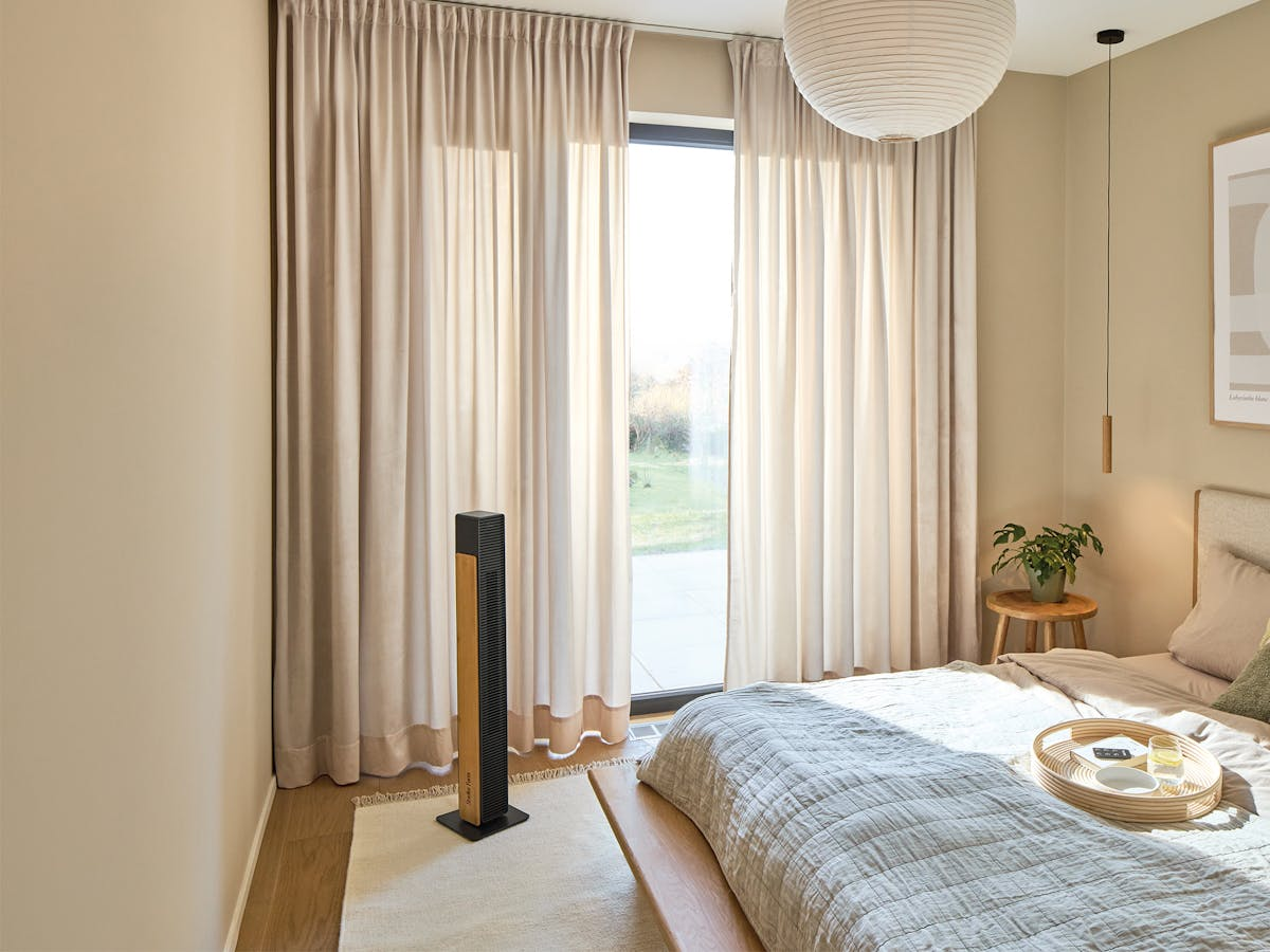 Ein Schlafzimmer mit einem Bett, einem Ventilator, Vorhängen und einem Fenster.