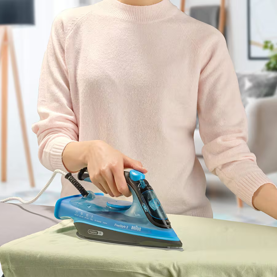 Una persona stira un tessuto verde chiaro con un ferro da stiro blu. Interno.