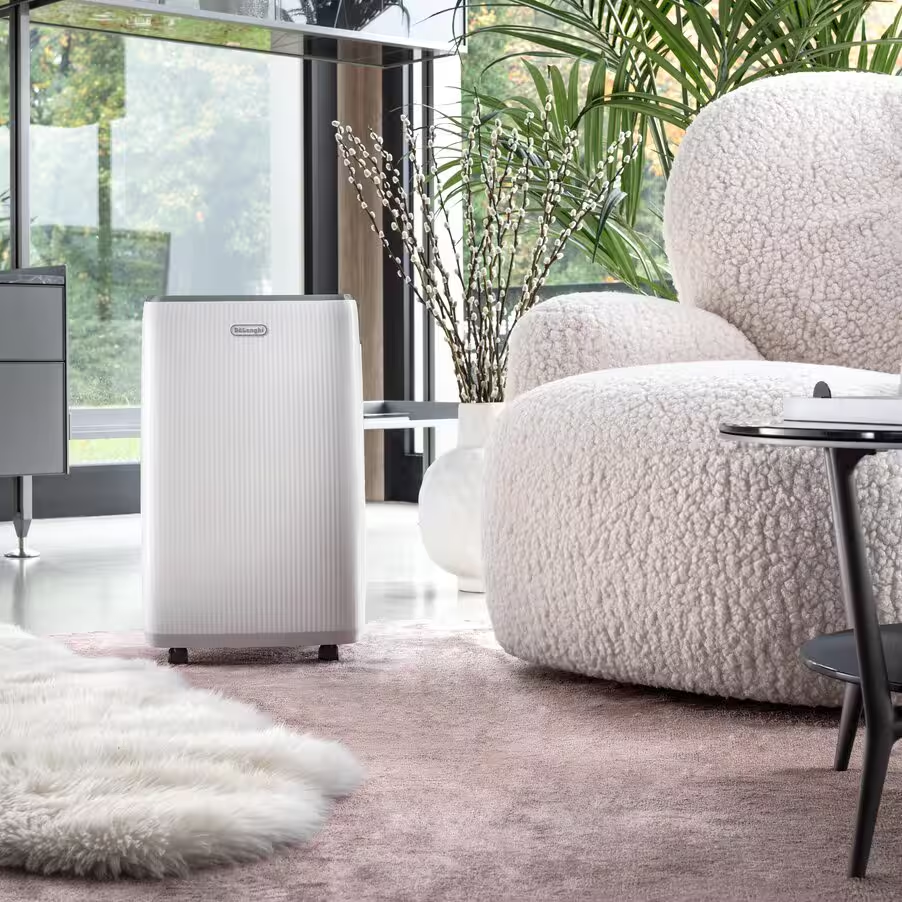 Un déshumidificateur blanc se tient sur un tapis rose à côté d'un fauteuil.