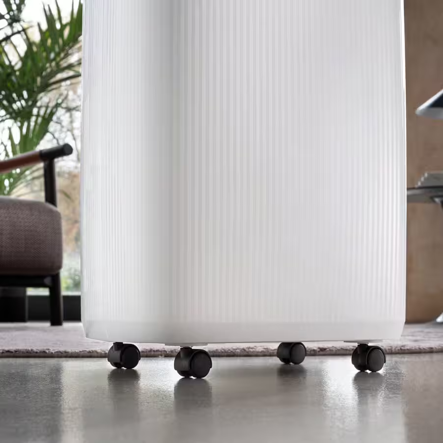 Un purificateur d'air blanc sur roulettes sur un tapis, à côté d'un fauteuil.