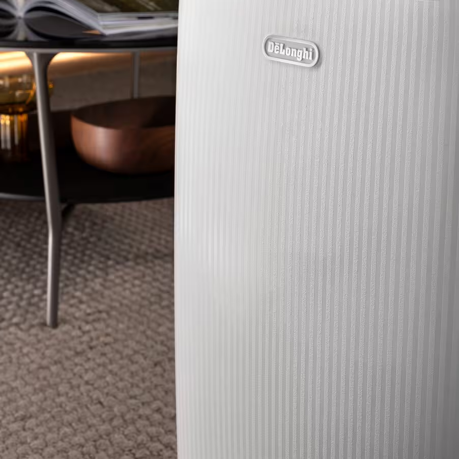 Un appareil blanc à nervures verticales et logo Delonghi. Une table avec des livres et un bol à côté.
