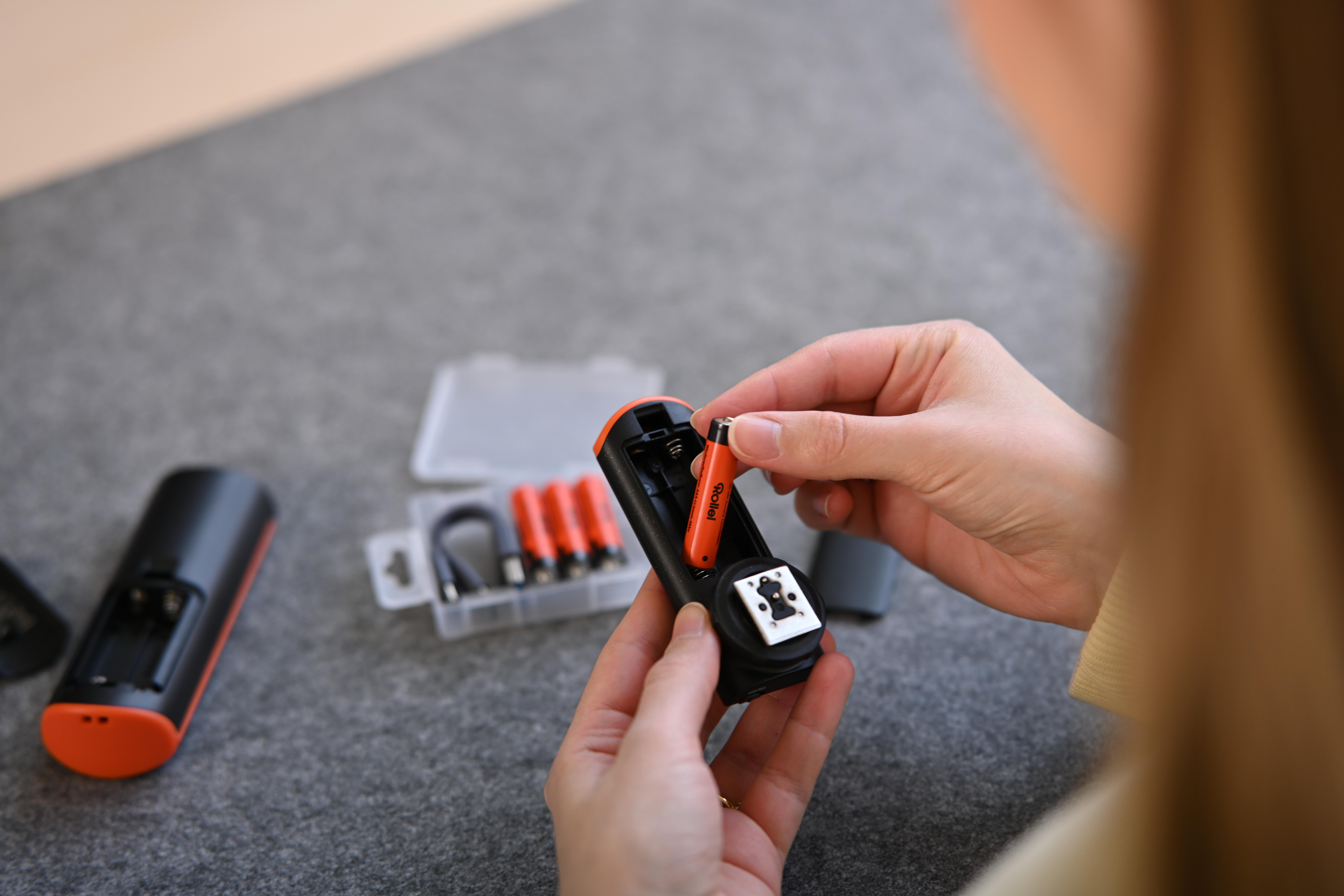Eine Hand setzt eine orangefarbene AA-Batterie in ein schwarzes Gerät ein.