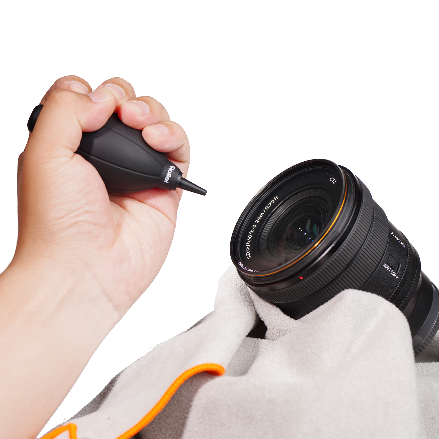 Hand hält schwarze Blasebalg-Birne nahe Sony-Kamerobjektiv auf Reinigungstuch.