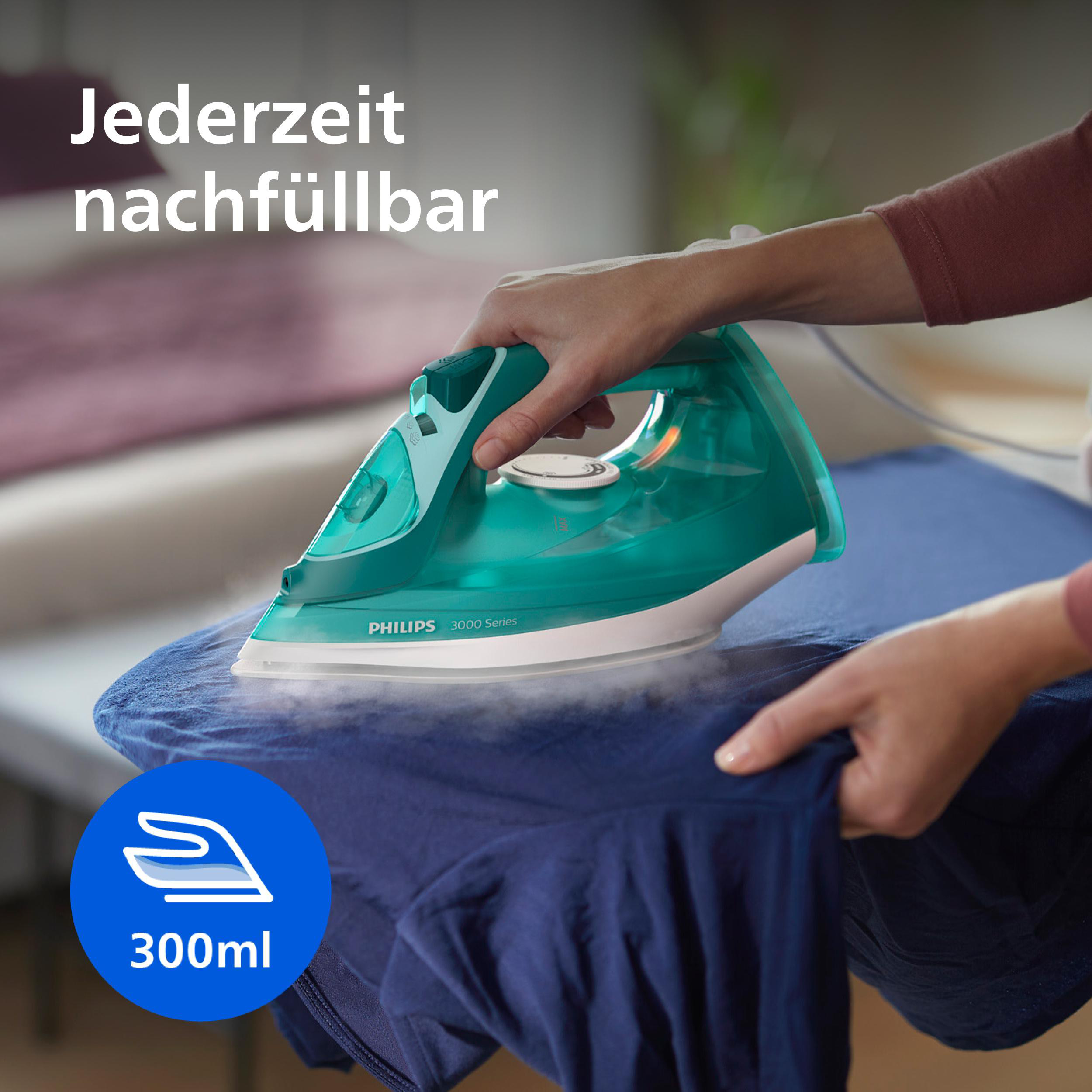 Eine Hand benutzt ein grünes Dampfbügeleisen auf einem blauen Stoff. 300ml.