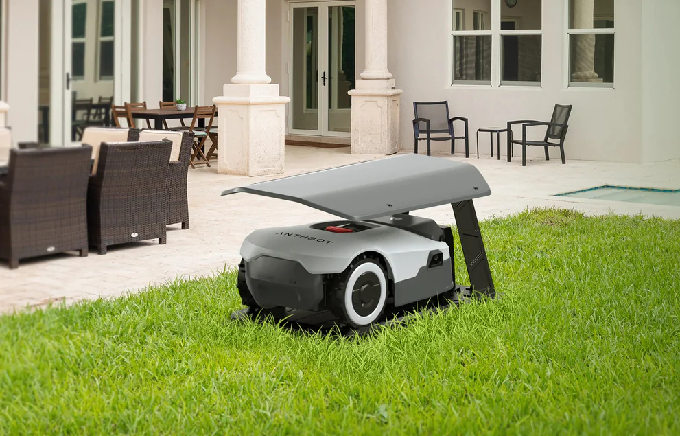 Ein Mähroboter steht auf einem grünen Rasen vor einem Haus mit Terrassenmöbeln.