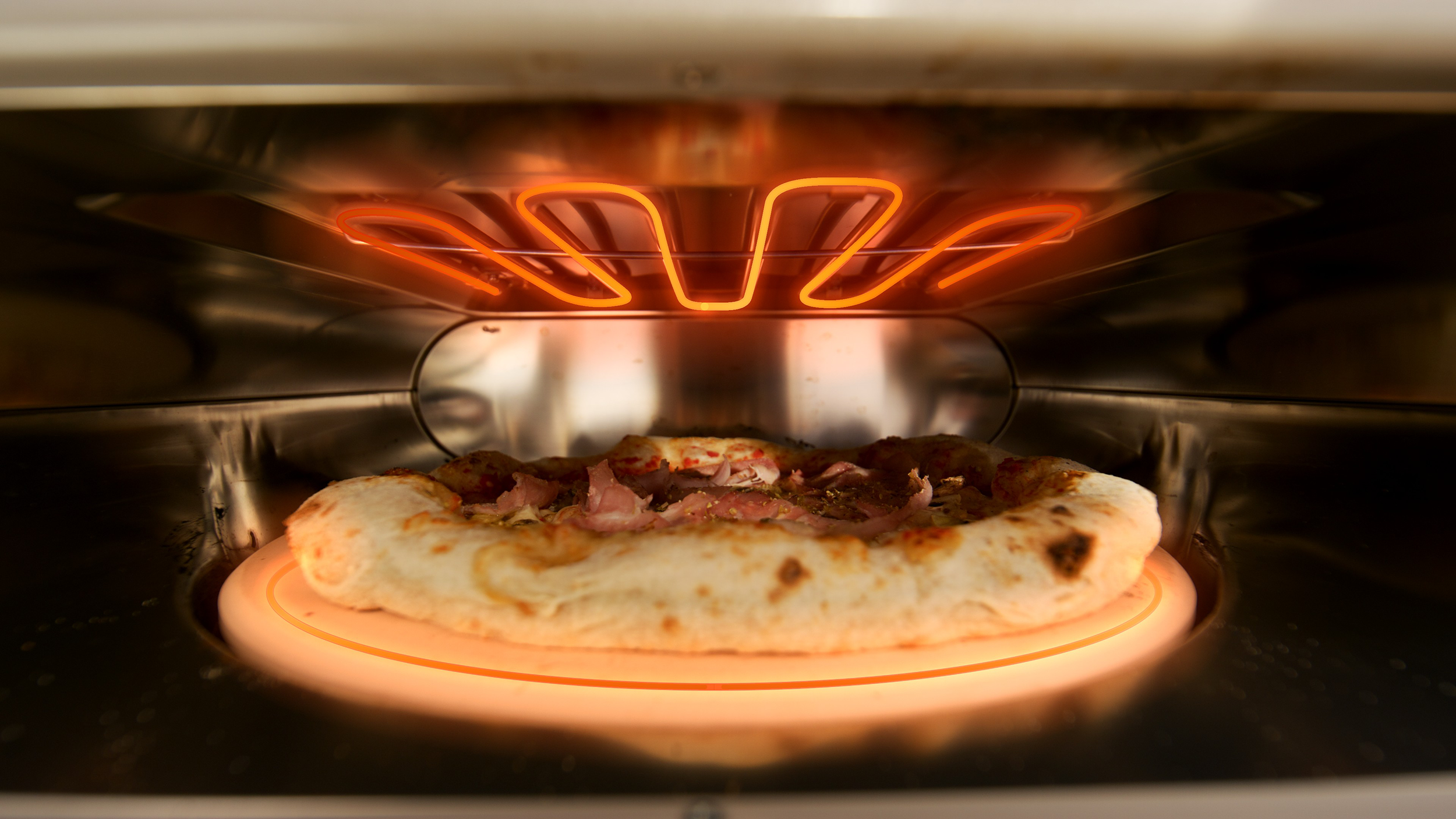 Egy sonkás pizza világító sütőben sül.