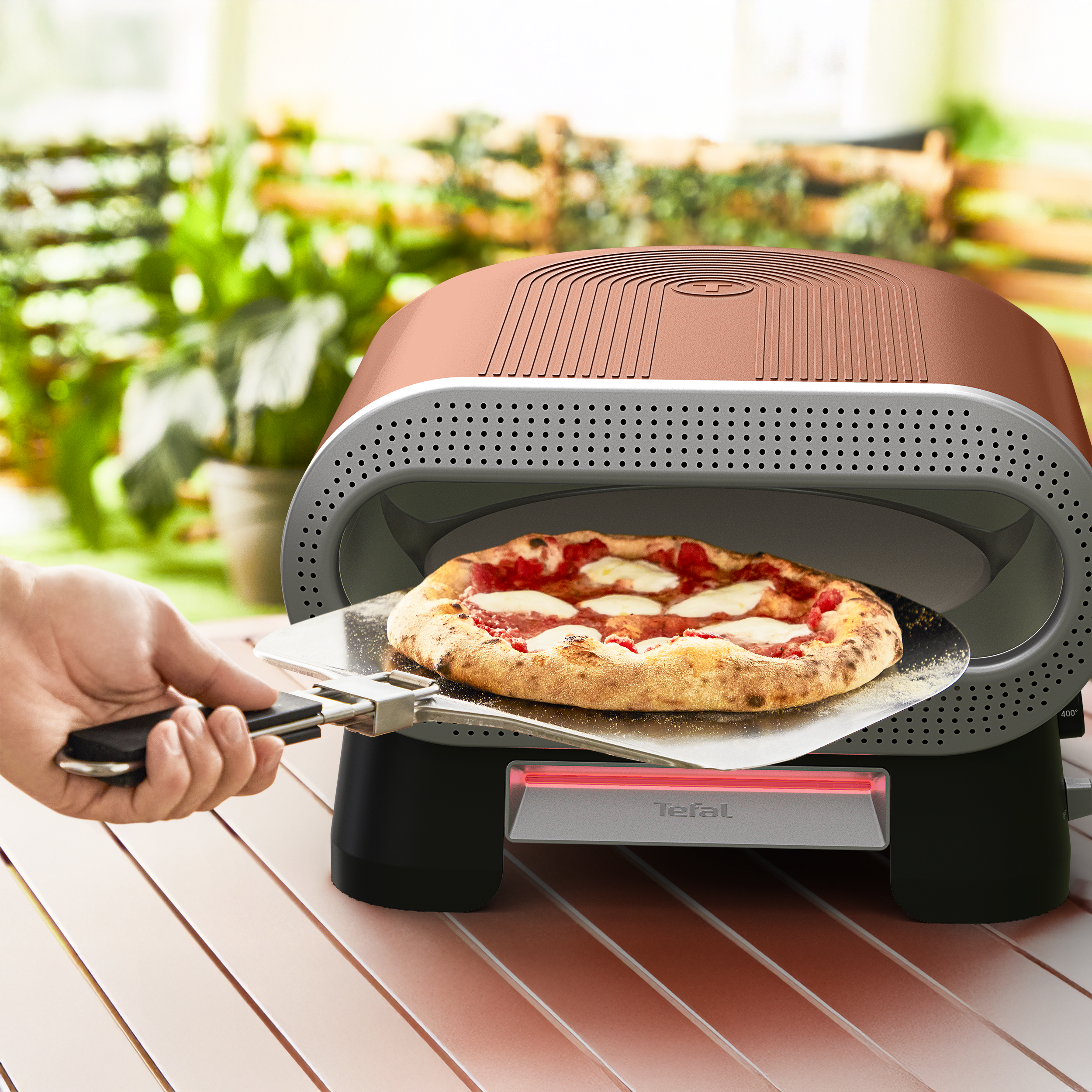 Egy kéz egy margherita pizzát tol be mozzarellával és paradicsommal egy pizza sütőbe.