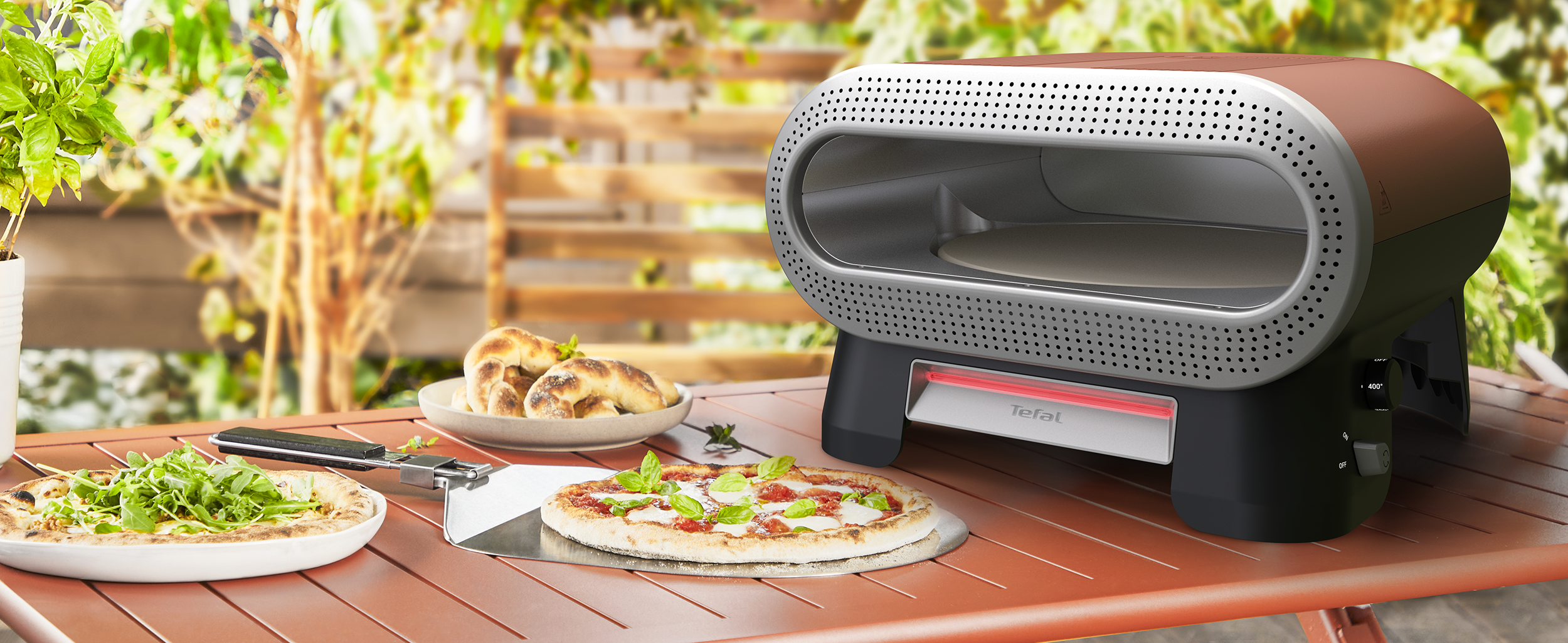 Egy Tefal pizzasütő áll egy asztalon két pizzával és kenyérrel.