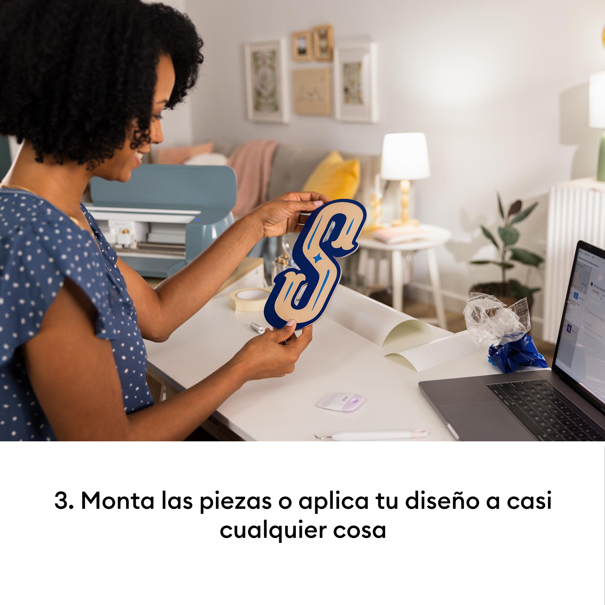 Una mujer sostiene una letra S azul y beige. Se ve una máquina de manualidades.