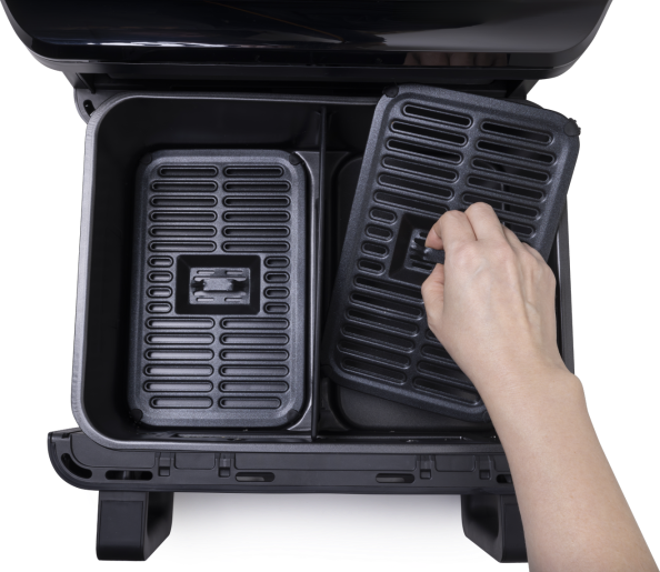 Kéz eltávolít egy fekete grill tálcát egy kétrekeszes air fryer kosárból.