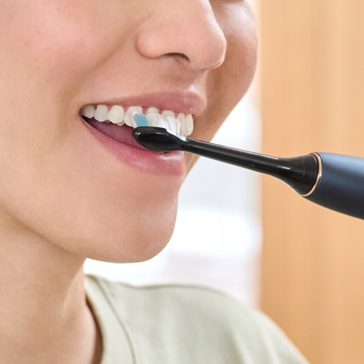 Zbliżenie na osobę myjącą zęby czarną szczoteczką elektryczną.