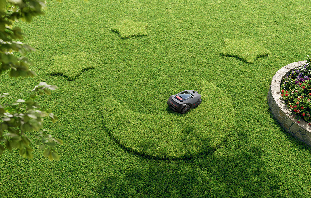 Robot koszący trawę tworzy na trawniku kształt półksiężyca, z gwiazdami i kwiatami.