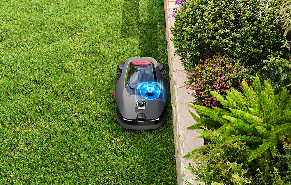 Robot koszący na zielonej trawie obok kamiennej ścieżki i kwiatów.