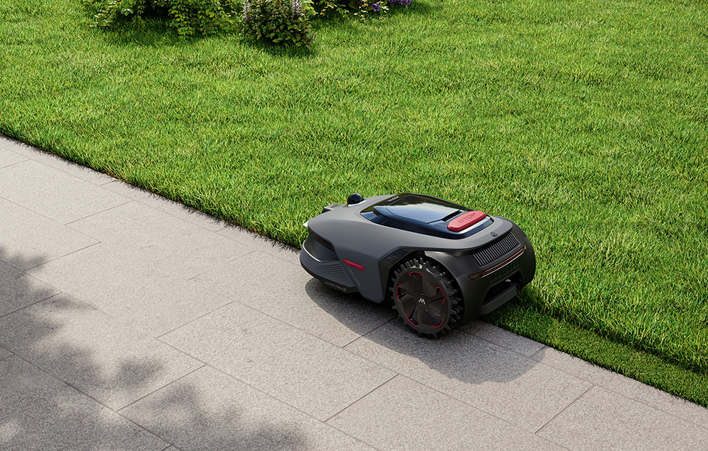Szara kosiarka automatyczna stoi na brukowanej ścieżce obok idealnie przystrzyżonego trawnika.