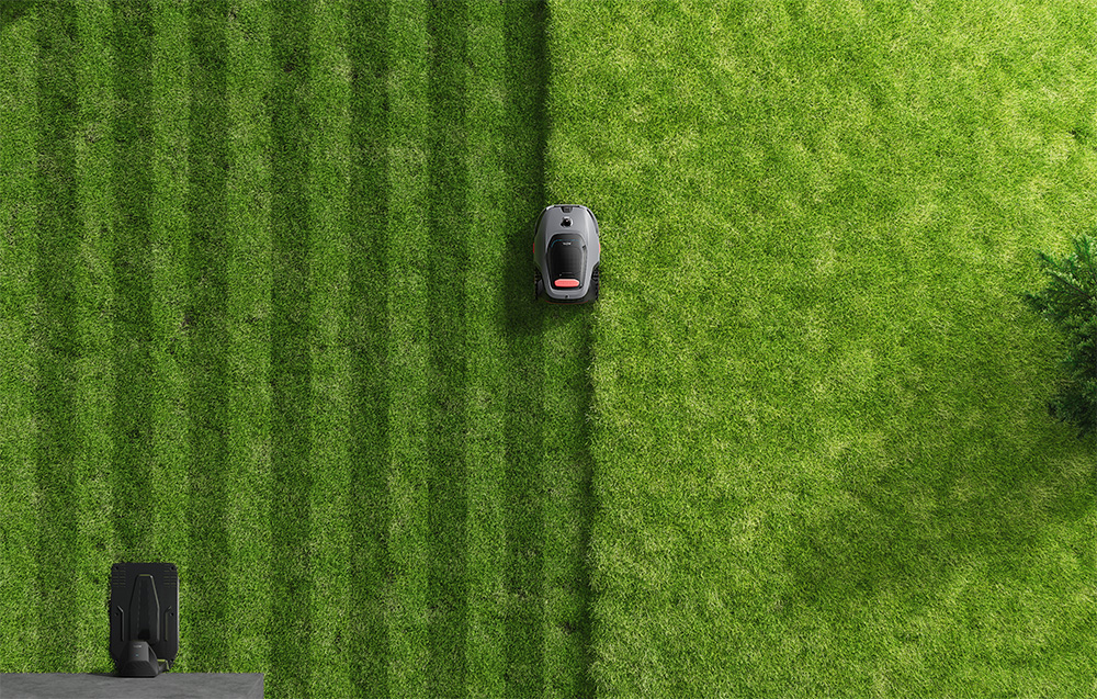Robot koszący przycina trawnik w paski. Stacja ładująca jest po lewej stronie.