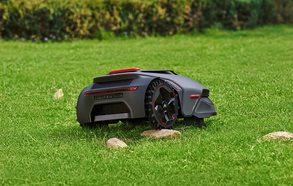 Ciemny robot koszący z czerwonymi akcentami stoi na zielonym trawniku.