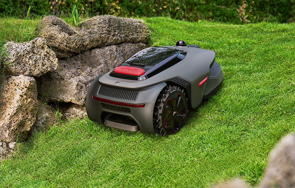 Szary robot koszący stoi na zielonym trawniku obok skał.
