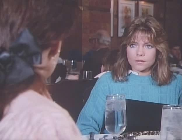 Eine Frau in einem blauen Pullover sitzt an einem Tisch mit einem Glas Wasser.