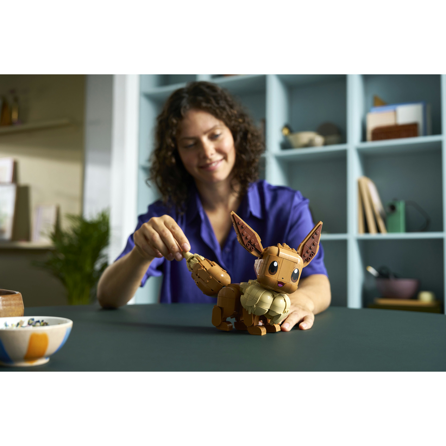Una donna costruisce una figura marrone di Eevee con mattoncini LEGO.