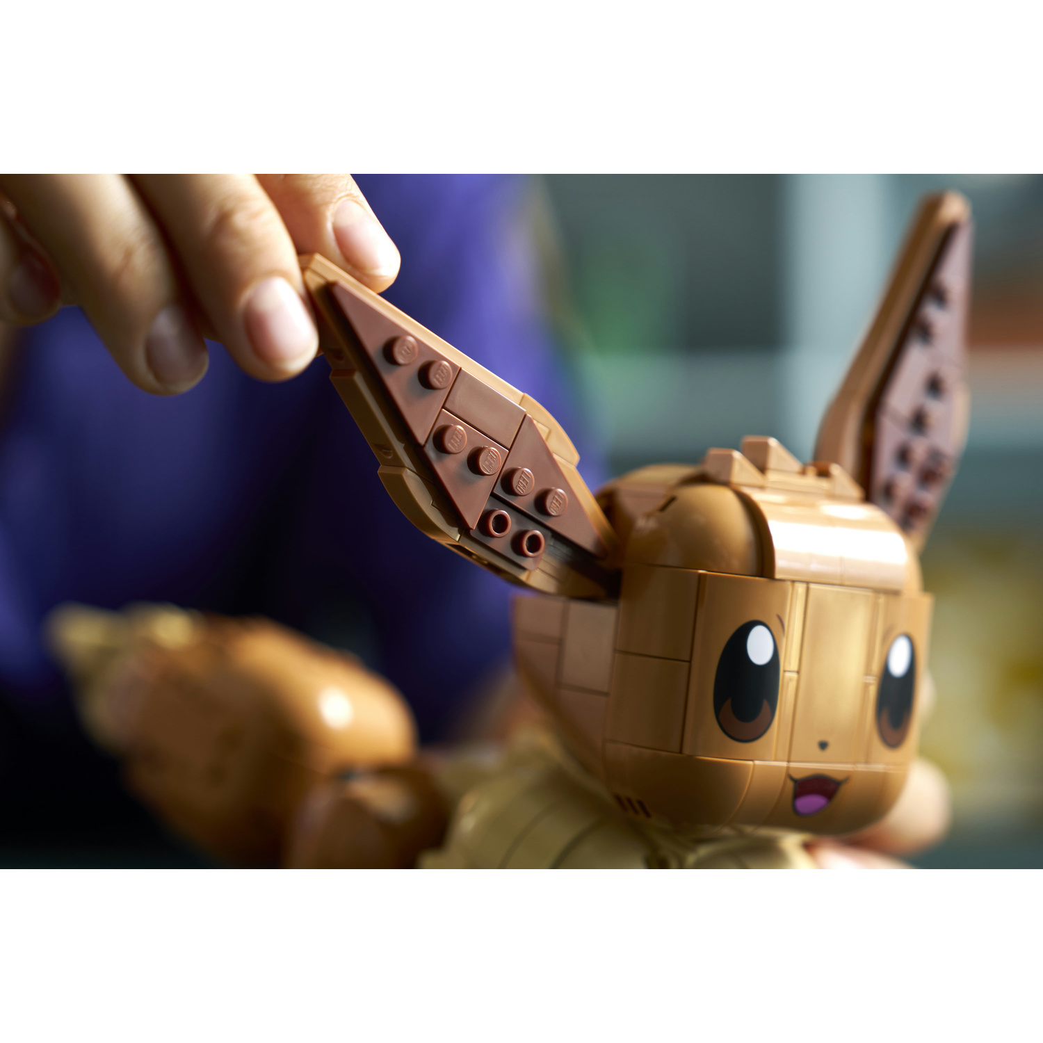 Una mano assembla un modello Eevee Lego marrone. Ripresa ravvicinata.