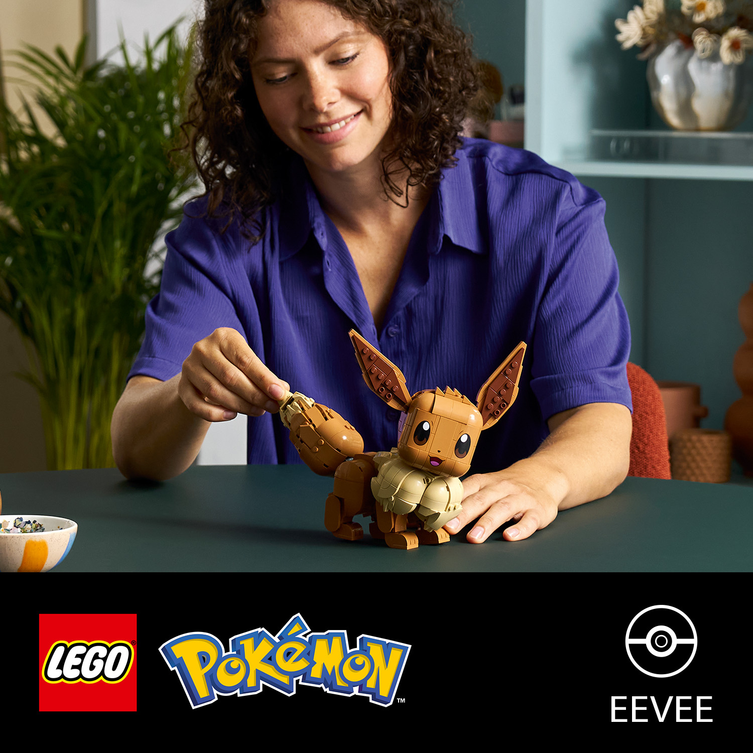 Donna costruisce una figura marrone di Eevee Lego su un tavolo.