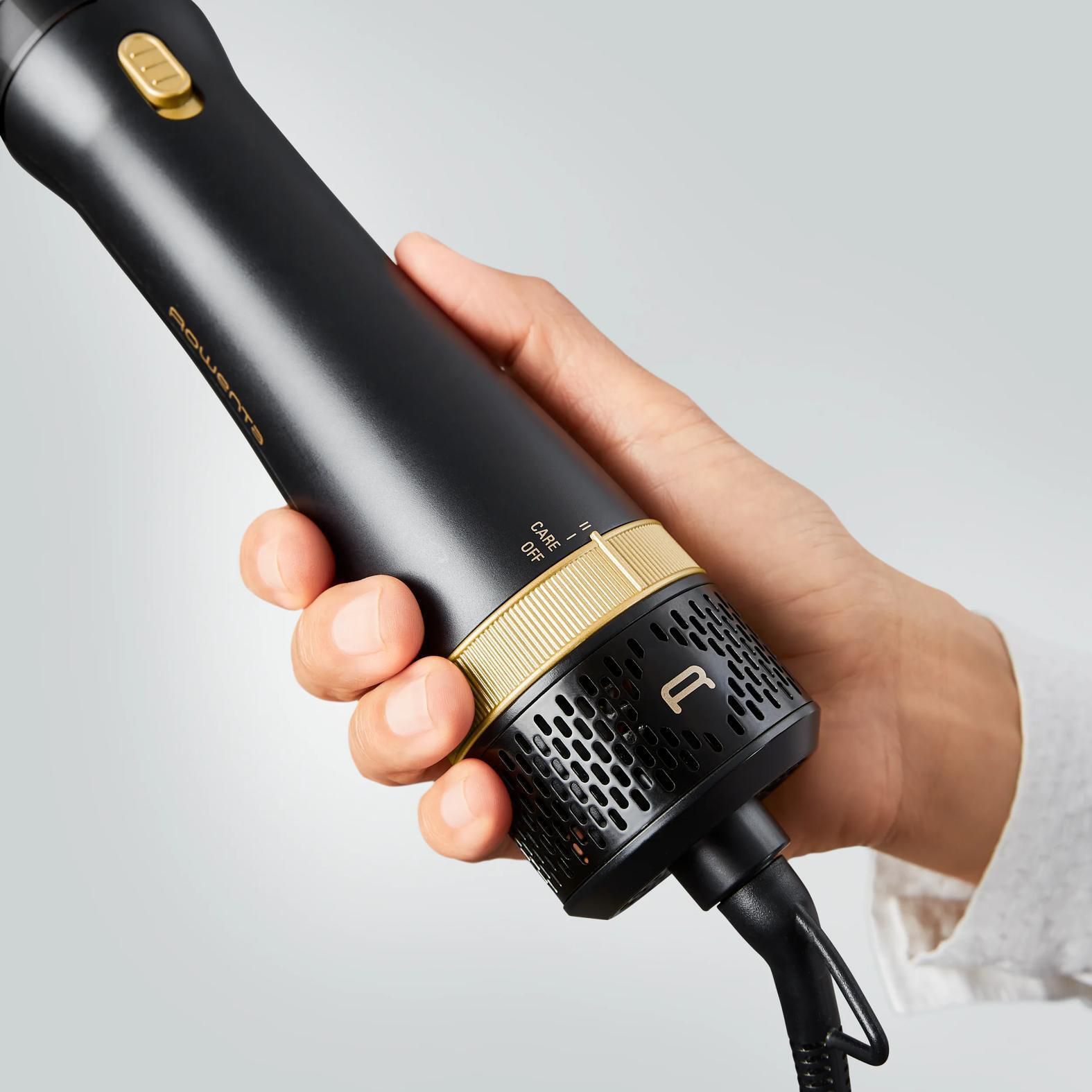 Hand hält schwarzen Haartrockner mit goldenen Akzenten und einem "R"-Logo.