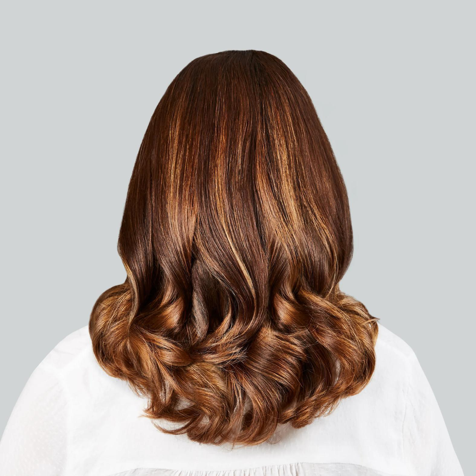 Rückansicht einer Frau mit langen, braunen Haaren mit goldenen Strähnen, gewellt.