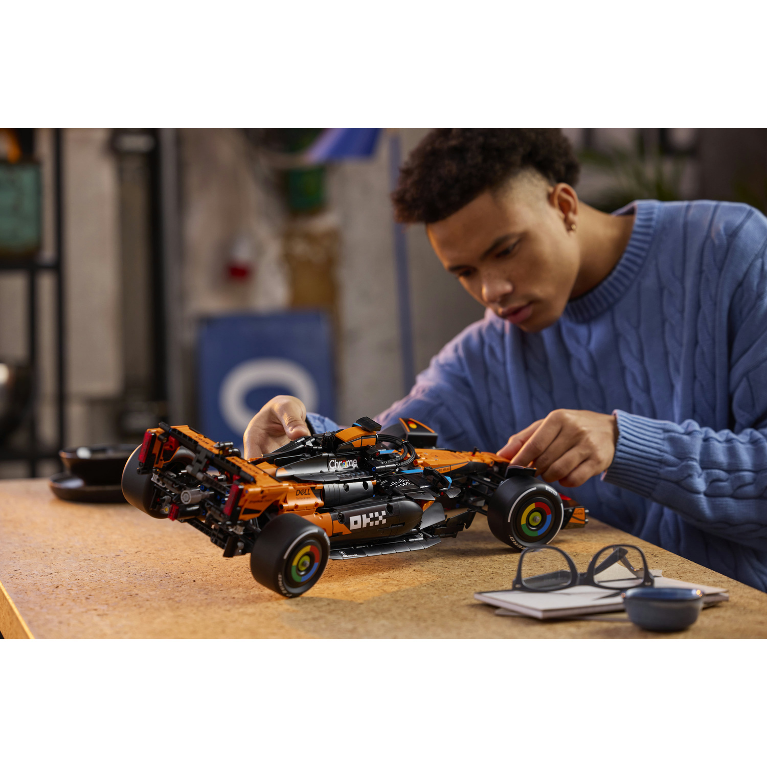 Un giovane costruisce un'auto da corsa Lego arancione su un tavolo.