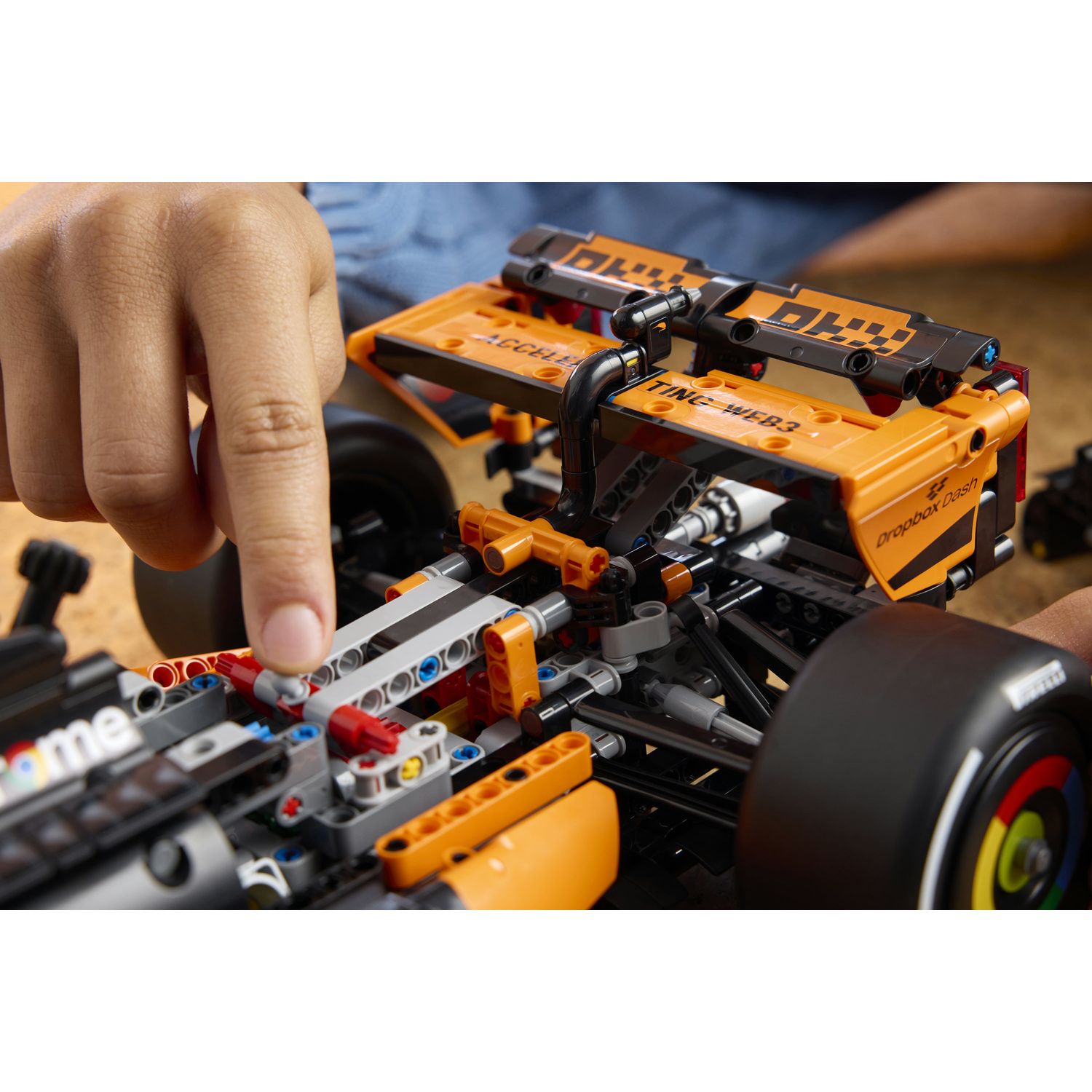 La mano di un bambino manipola un'auto da corsa LEGO Technic dettagliata arancione e nera.