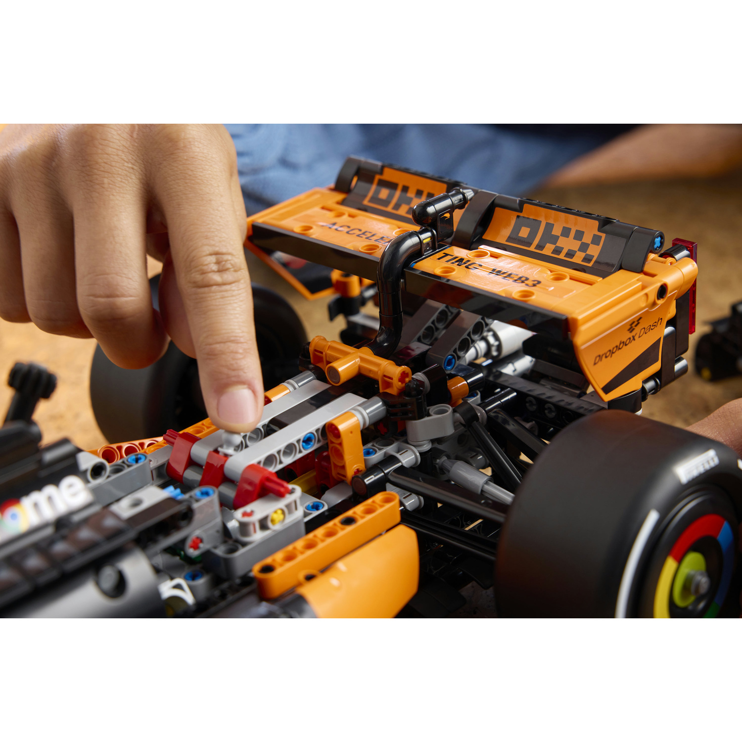 Un dito tocca un'auto da corsa Lego arancione e nera in costruzione.