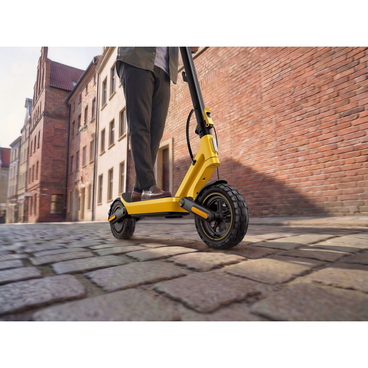 A person rides a yellow electric scooter on a cobblestone street in a city.
