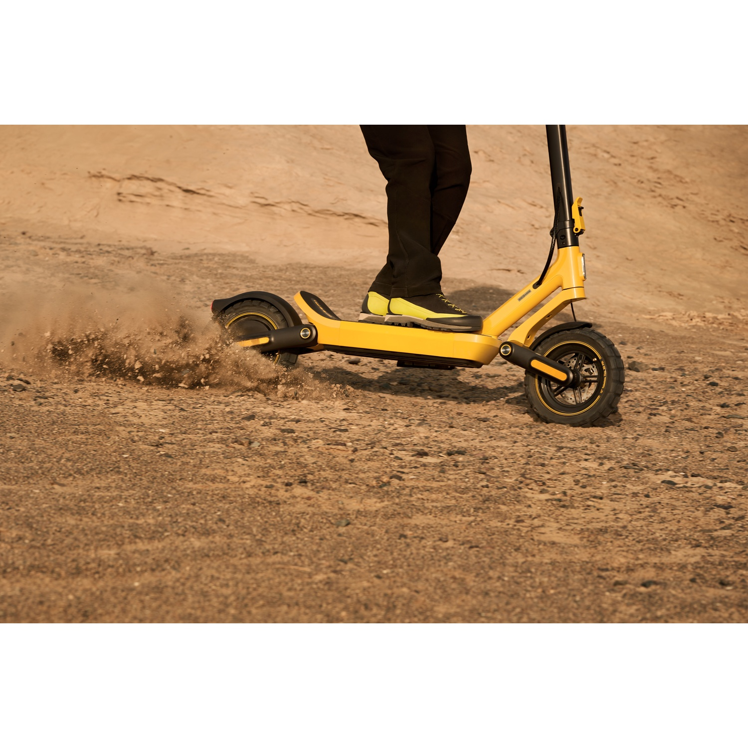 Yellow electric scooter rides on a dusty, uneven road. High resolution.