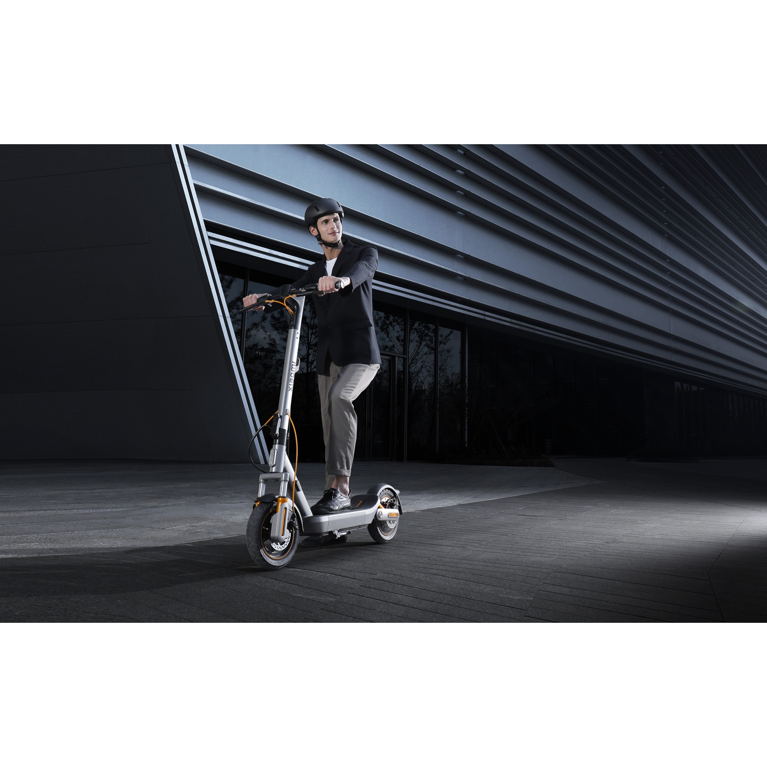 Man in helmet rides e-scooter in front of modern building.