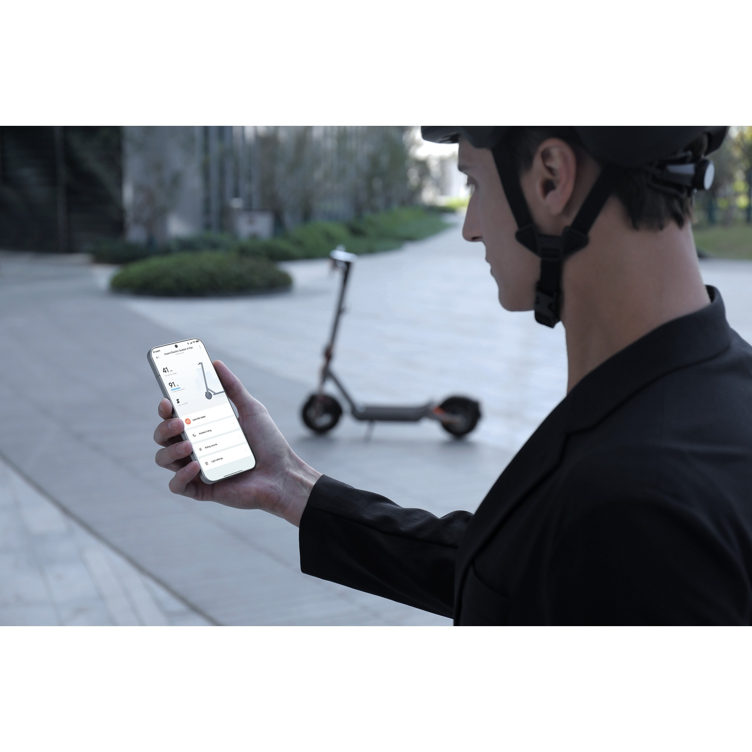 Man in helmet holds phone with e-scooter app, e-scooter in background.