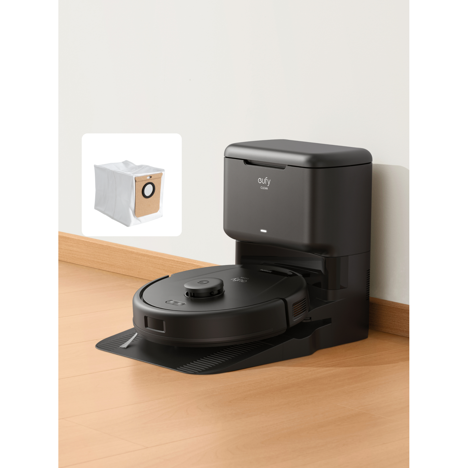 A black robot vacuum is on a charging dock next to a white dust bag.