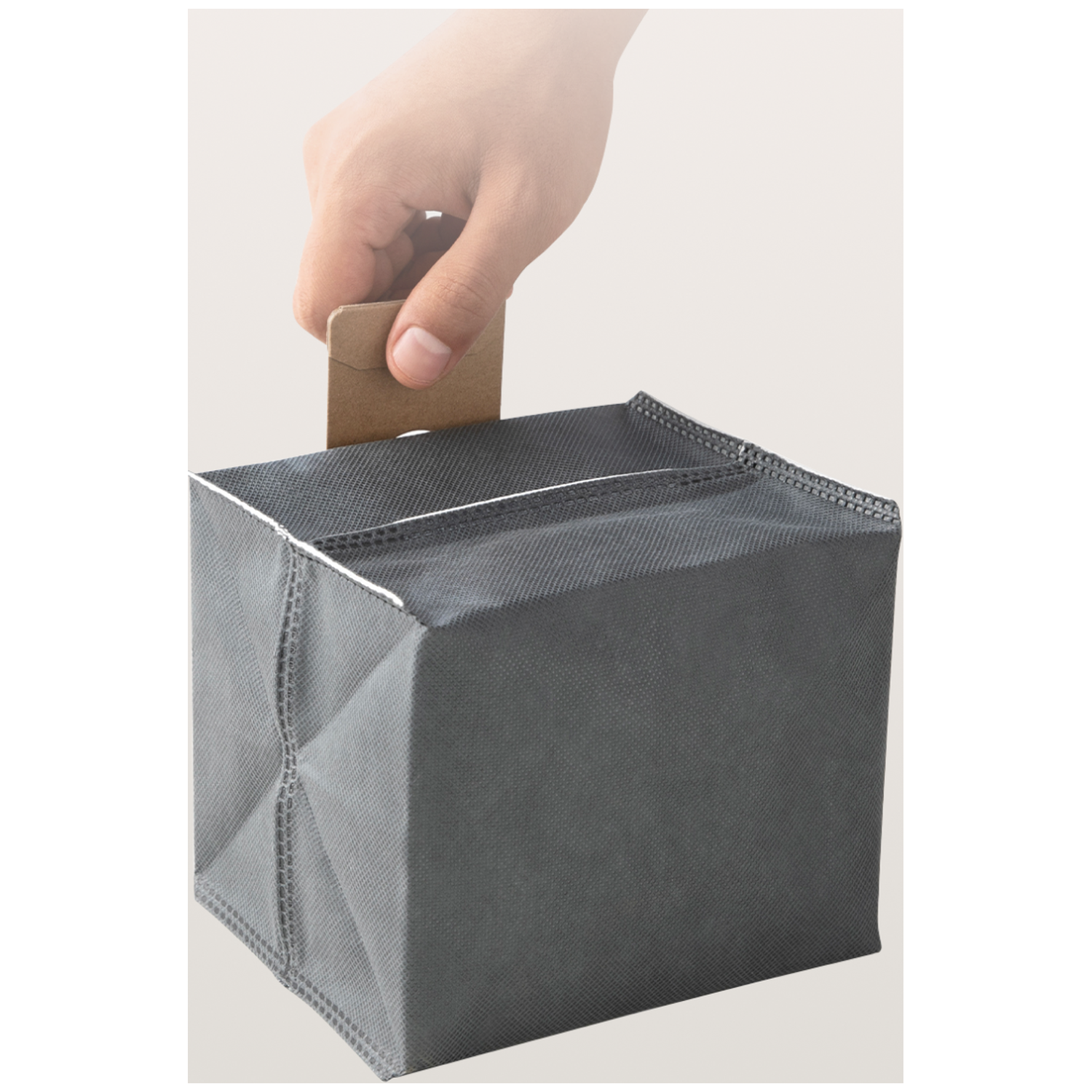A hand inserts a small brown card into a gray fabric cube.